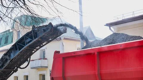 Road milling machine loading asphalt grit into dump truck for urban pavement Stock Photos