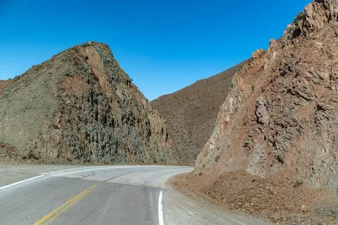 Road in the mountains between the cliffs overlooking the snowy hills Stock Photos