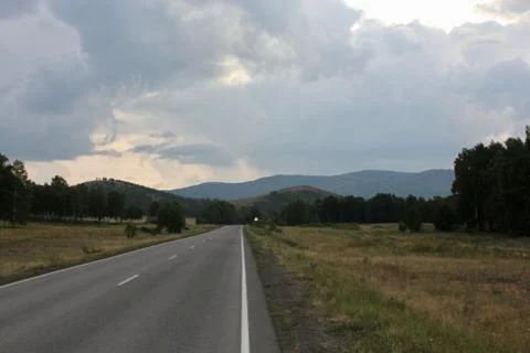 A road in the mountains going far beyond the horizon at sunset Stock Photos