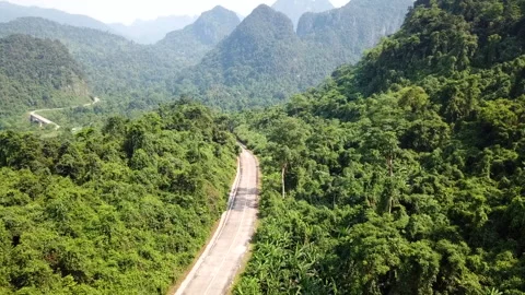 Road passing through a dense jungle with mountains in the background in Dong Hoi 스톡 동영상 144909749