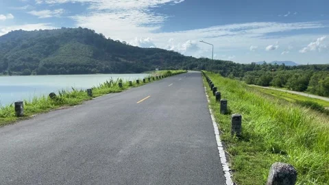 Road path at dam panning shot on a sunny day mountain blue sky tree Stock Footage 283171482