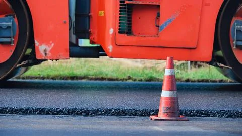 Road roller compacting new asphalt pavement with a traffic cone during roadwork Stock Photos