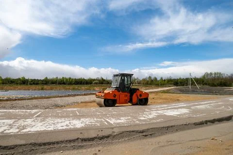 A road roller is on a construction site by a water area with light clouds a.. Stock Photos