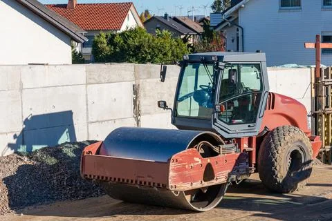 Road roller standing on a construction site near a concrete fence. Stock Photos