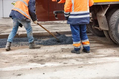 Road service workers level fresh asphalt with a shovel for patching the road. Stock Photos