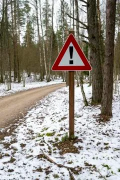 Road sign triangular shape with exclamation mark. Winter road in forest. Stock Photos