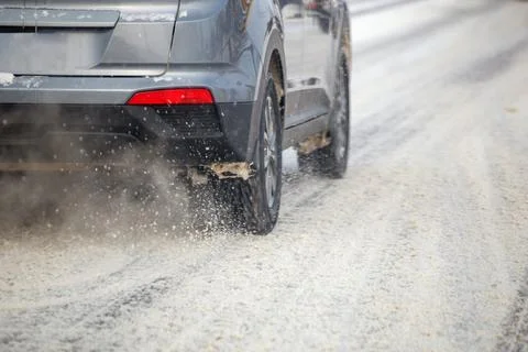 Road snow flinders flow from wheels of gray car moving fast in daylight city Фото