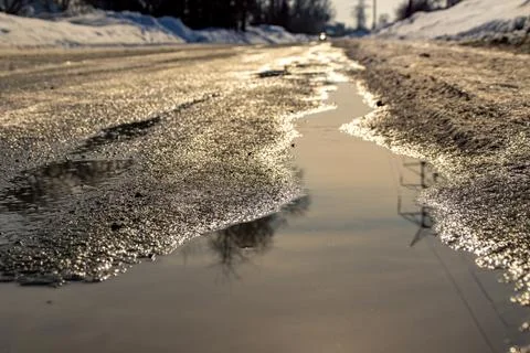 Road with spring streams that flow along the road covered with ice and heavy  Stock Photos
