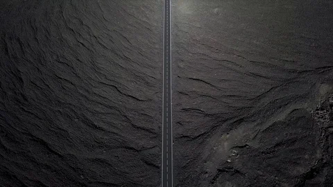The road  is surrounded by black volcanic lava. Top view. Minimalistic landscape Stock Footage 100657450