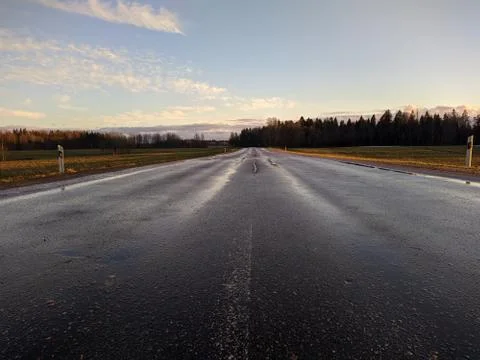 Road surrounded by fields leading far beyond the horizon at evening Stock Photos