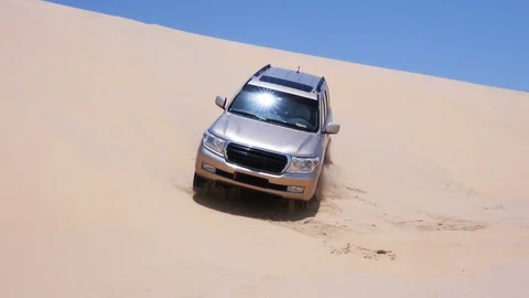 Off road SUV riding over crest of sand dune Stock Footage 76936050