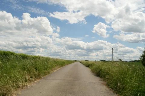 A road with a tall windmill in the background Stock Photos