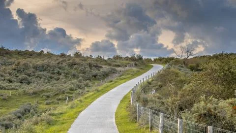 Road through dunes with clouds Stock Photos