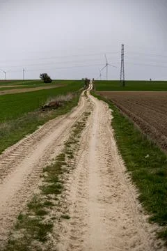 Road through fields in rural area during cloudy day at the beginning of sprin Stock Photos