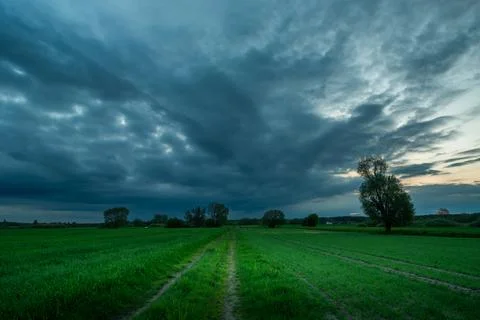 Road through green fields and rainy clouds Stock Photos