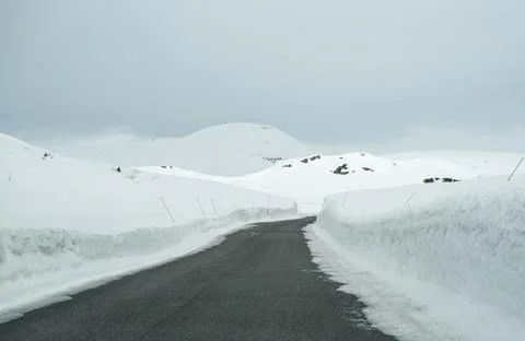 Road through a mountain pass with deep snow towering up on both sides. Stock Photos