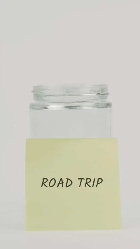 Road trip text or word on yellow sticky note attached to glass jar with hand Stock Footage 311782679