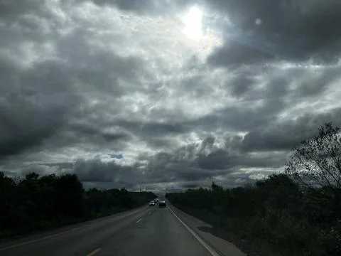 Road trip under dramatic cloudy sky with sun rays breaking through, cars on.. Stock Photos