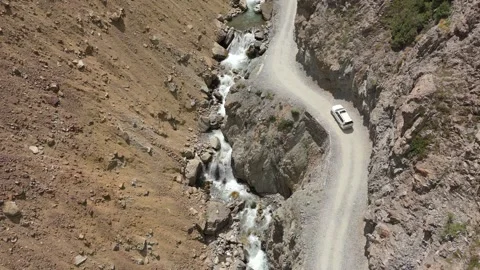 Off road vehicle moving on winding cliffside trail next to a cascading river 스톡 동영상 345000547