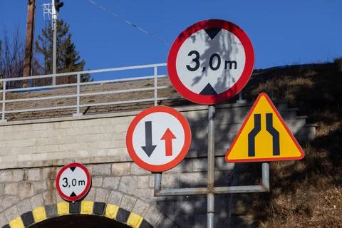 Road warning and priority signs mounted near a narrow stone tunnel entrance, Фото
