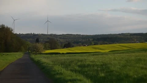 Road winding through a field with windmills in the distance against a cloudy sky Video stock 275556883