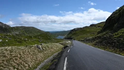 Road winds through green hills in Norway with a lake in the distance under .. Stock Footage 340209683