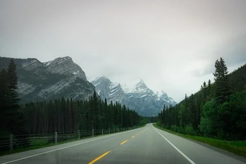 Road winds through a valley flanked by towering mountains Stock Photos