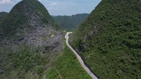 A road winds through a valley surrounded by towering mountains, under a vast sky Stock Footage 274262685