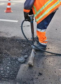 A road worker clears some of the asphalt with a jackhammer while repairing a  Stock Photos