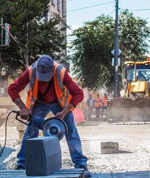 The road worker processes the stone with an electric saw. Stock Photos