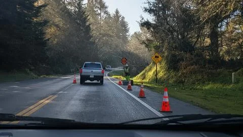 Road worker in reflective vest holds slow sign among orange cones Stock Photos