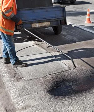 A road worker sprays a bitumen mixture onto the cleaned surface of the old as Stock Photos