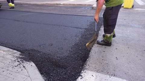 Road worker throwing fresh warm mix asphalt on the road during paving proces 스톡 동영상 253230755