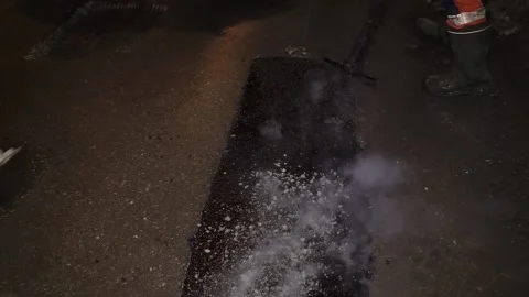 A road worker throws rubble on the hot liquid asphalt Stock Footage 150514067