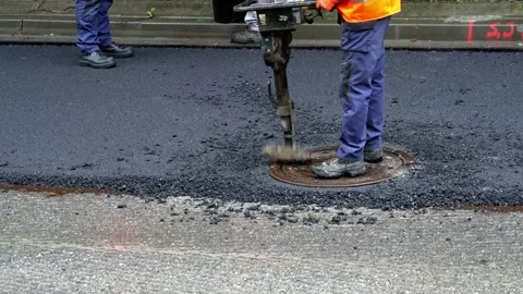 A road worker in uniform using a special tool lays a manhole cover on a well Stock Footage 204812754