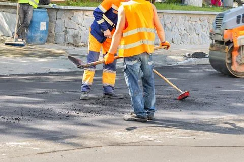 Road workers clean the asphalt pavement on the roadway with a brush and shove Stock Photos