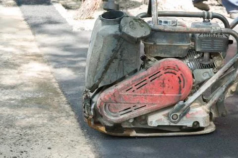 Road workers compact the asphalt with a vibrating rammer on the road. Worker  Stock Photos