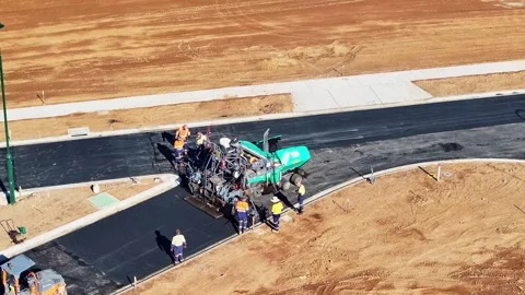 Road workers hard at work working hot bitumen behind a road paving machine Stock Footage 279354953