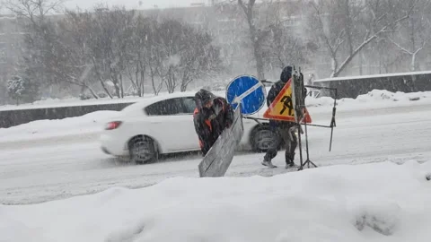 Road workers installing detour signs on city highway. Heavy snowfall in city Stockbeeldmateriaal 259996249