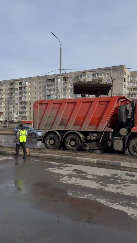 Road workers use backhoe loaders to collect icy mud, unload it into dump truck Stock Footage 306029540