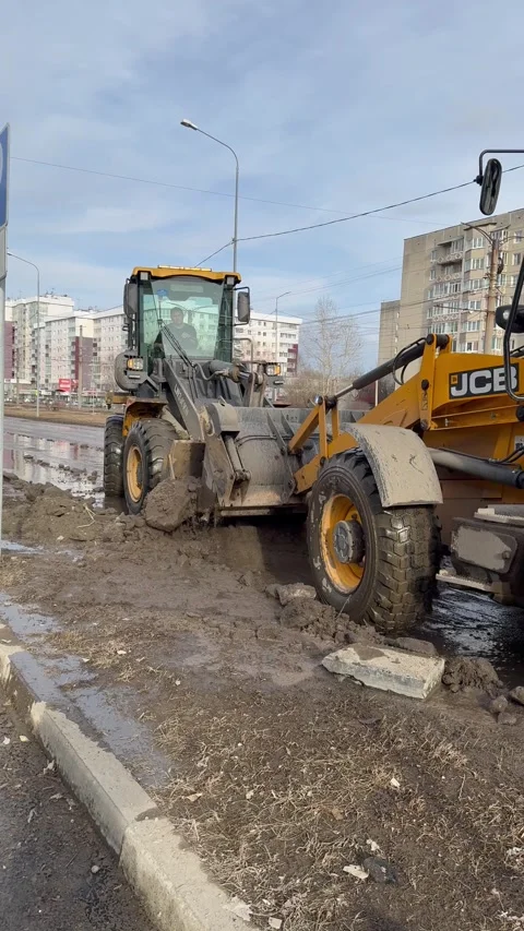 Road workers use excavators and loaders to collect icy mud from road in bucket Stock Footage 306029550