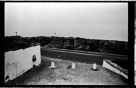 Roadside Cross and Stone Cliffs Along a Foggy Portuguese Coastal Road 库存照片