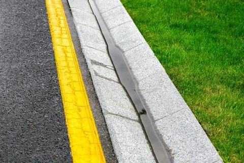 Roadside drainage system tray with flowing rain water on an asphalt road. Stock Photos