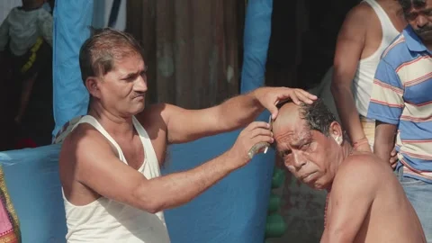 Roadside local barber is shaving head of Hindu male devotee outside Ganges River Stock Footage 264021949