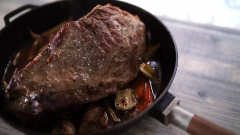 Roast beef with vegetables in a pan steaming on a wooden table Stock Footage 287403756