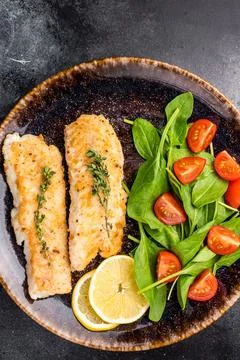 Roast Cod fish fiilets, white fish meat on plate with salad. Black backgrou.. Stock Photos