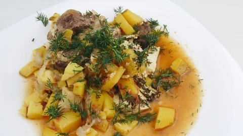Roast potatoes beef stew topped with greens on a white plate. Stock-Footage 127367336
