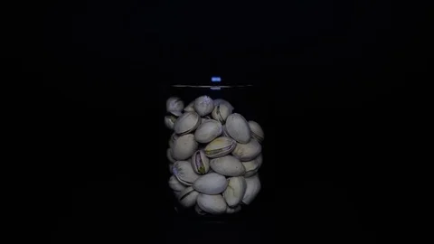 Roasted and salted pistachios in shells in transparent glass on black background Vidéo 75892015