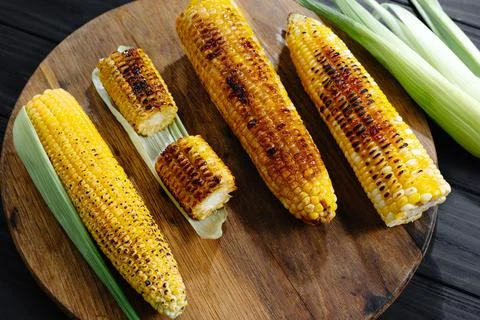 Roasted barbecue corn. Grilled corn on a dark wooden background. Slices of Stock Photos
