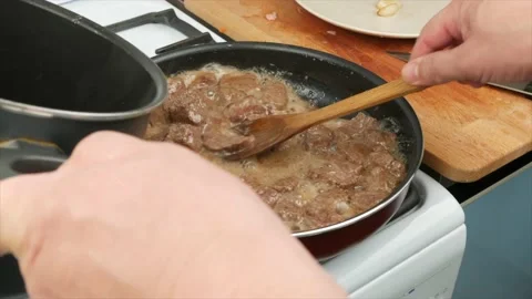 Roasted beef meat is removed from the pan into a stew pan, close-up, wooden s Stock Footage 133715018